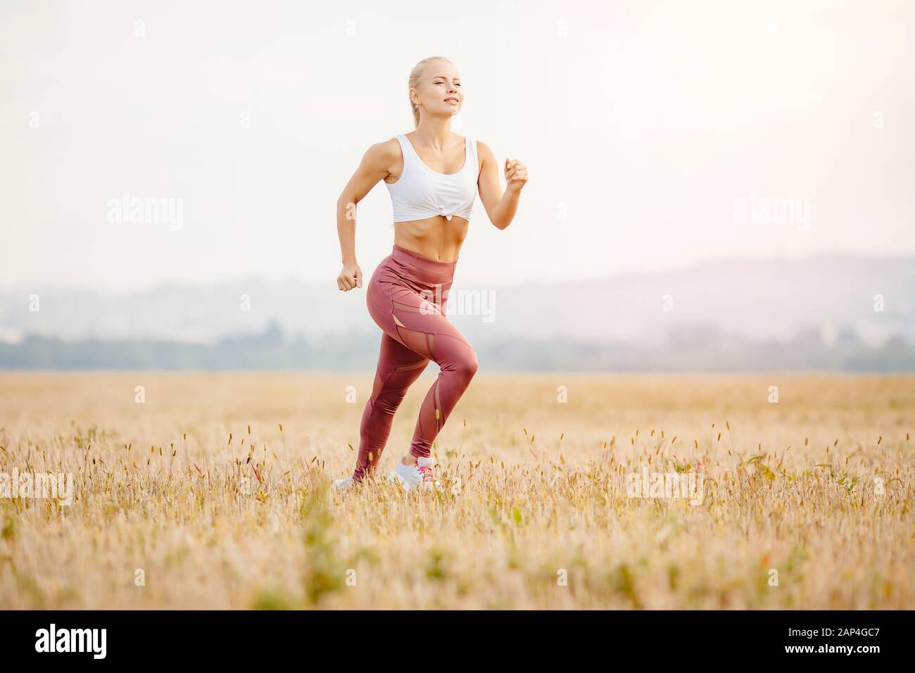 Fluttering dei capelli nella ragazza bionda del vento corridore alba, workout di concetto Foto Stock