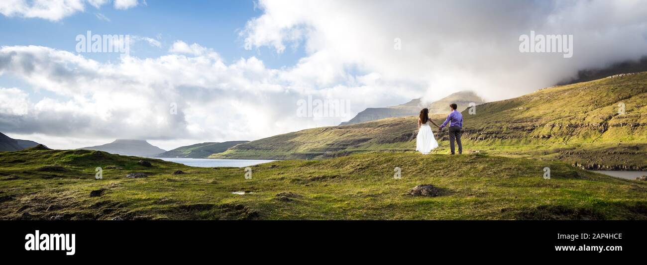 Una coppia felice in abiti da sposa o la sposa e lo sposo tenendo le mani e guardando la natura pittoresca. Isole Faroe/ Foto Stock