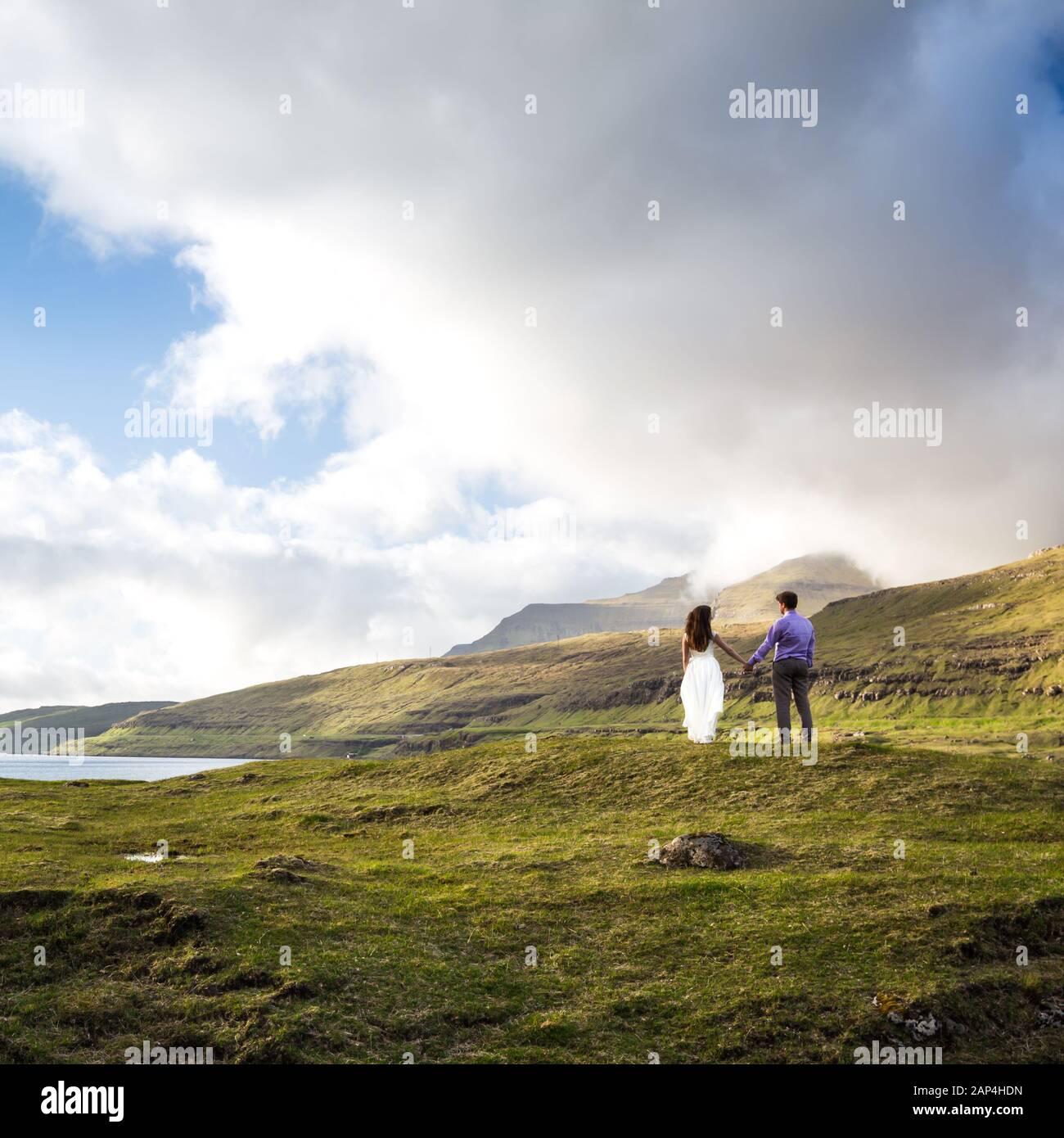 Una coppia felice in abiti da sposa o la sposa e lo sposo tenendo le mani e guardando la natura pittoresca. Isole Faroe/ Foto Stock