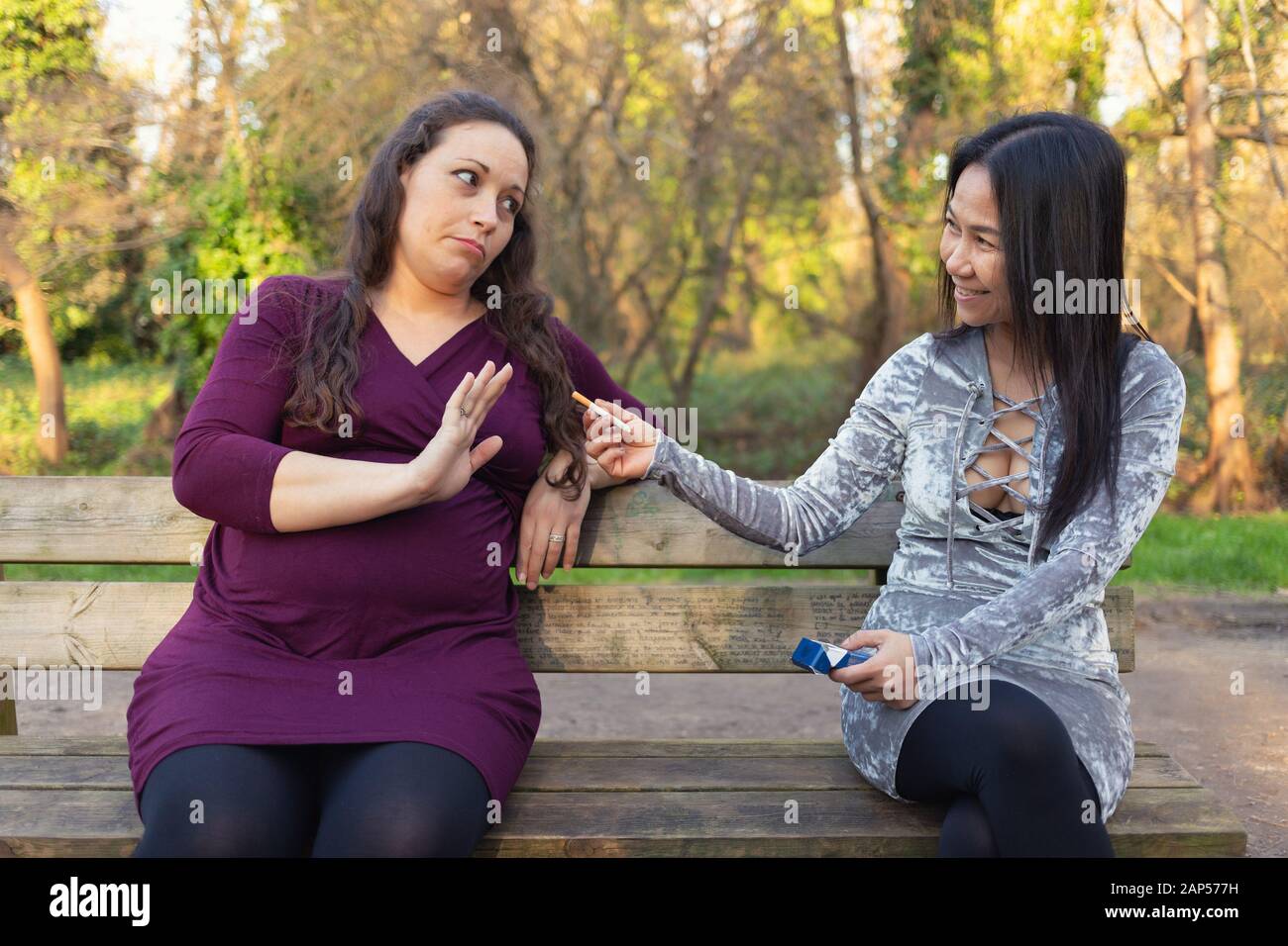 Donna incinta seduto sulla panchina del parco e rifiutando la sigaretta offerti dalla sua amica . Evitando cattive abitudini e gravidanza sana behaviou Foto Stock