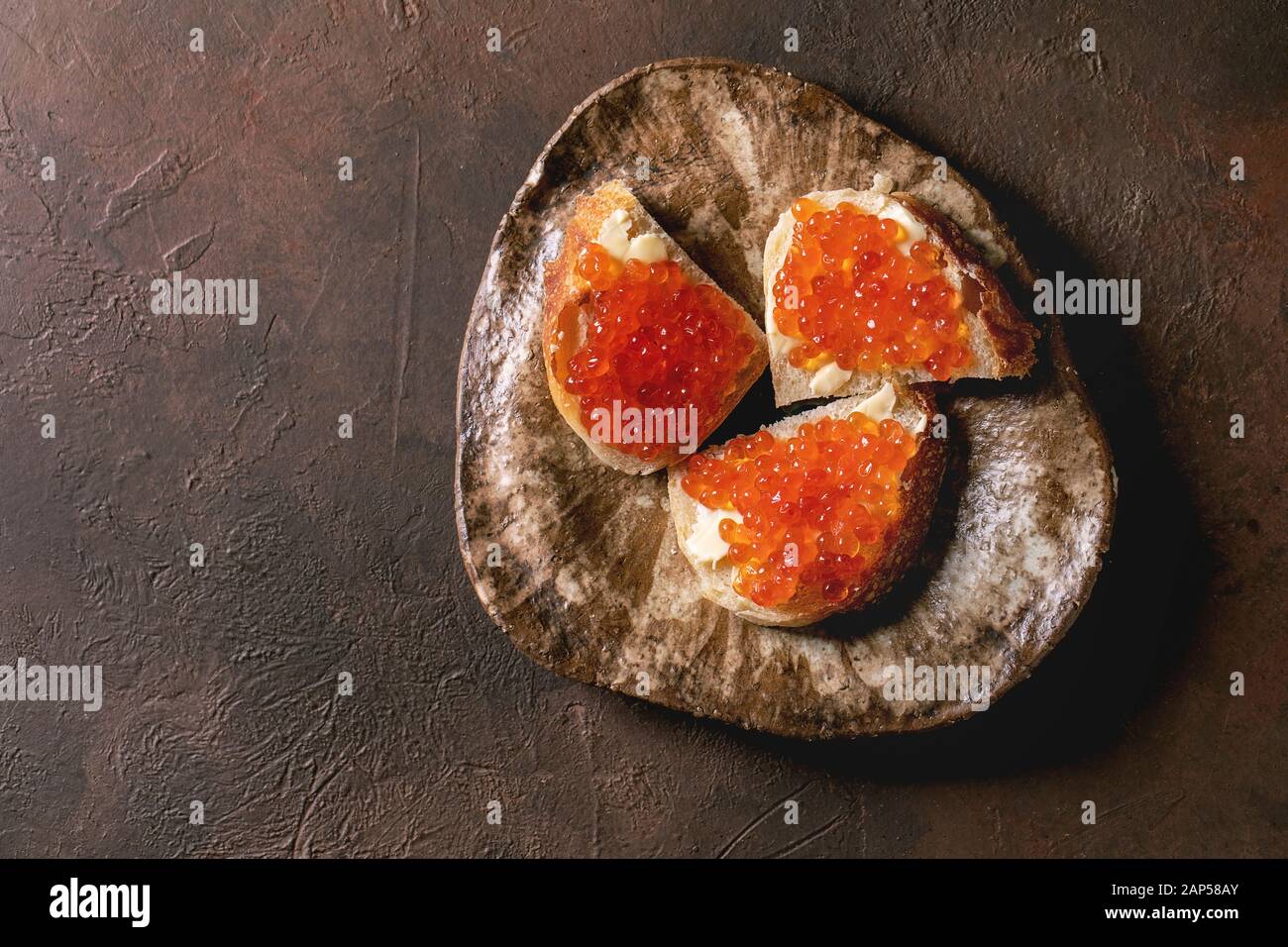 Rosso Salmone caviale sul pane con burro sulla piastra in ceramica oltre marrone scuro dello sfondo texture. Laici piana, spazio Foto Stock