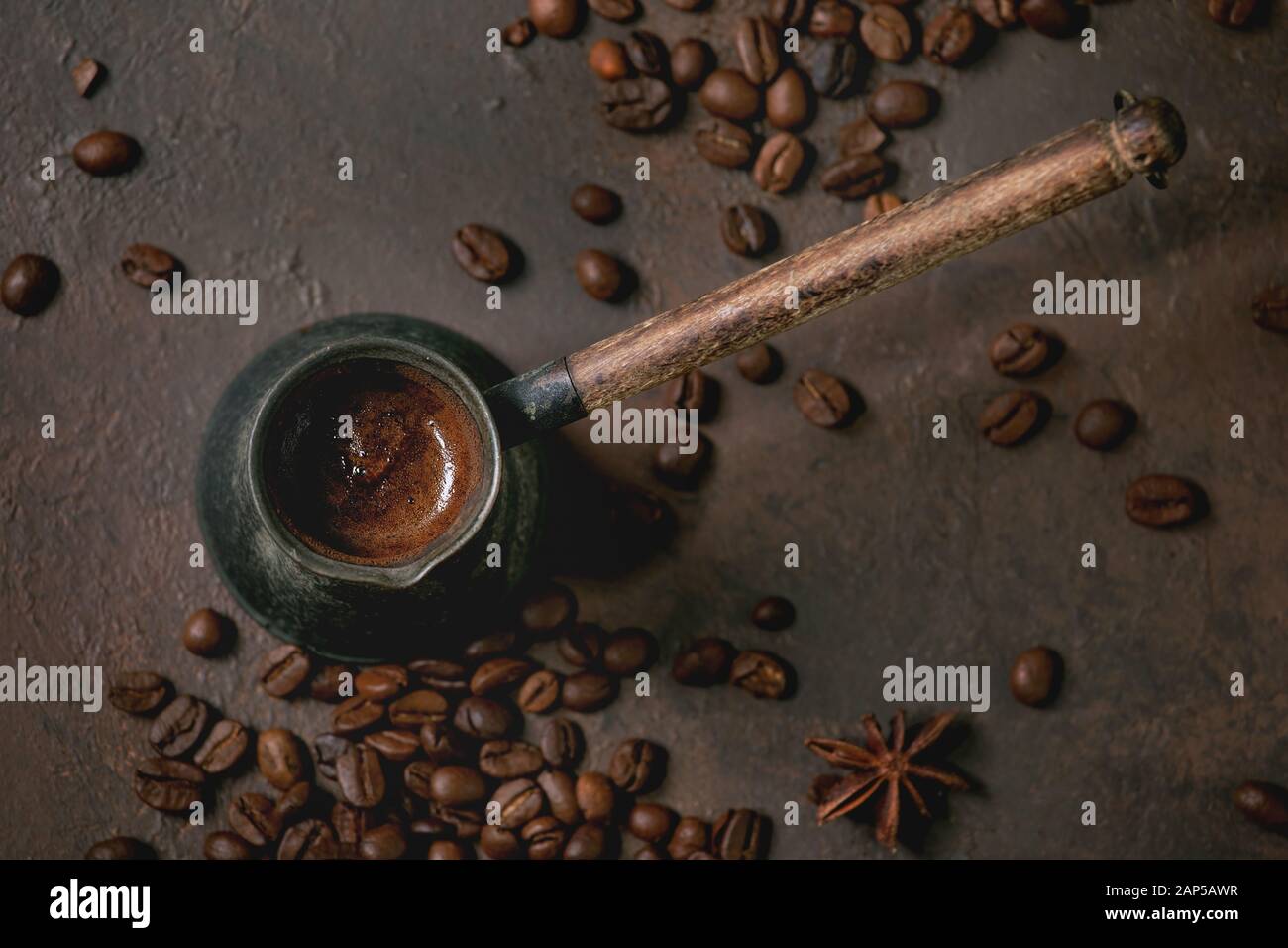 Nero caffè turco con schiuma nel vecchio cezve vintage POT del caffè torrefatto fagioli come sopra in marrone sfondo texture. Laici piana, spazio Foto Stock