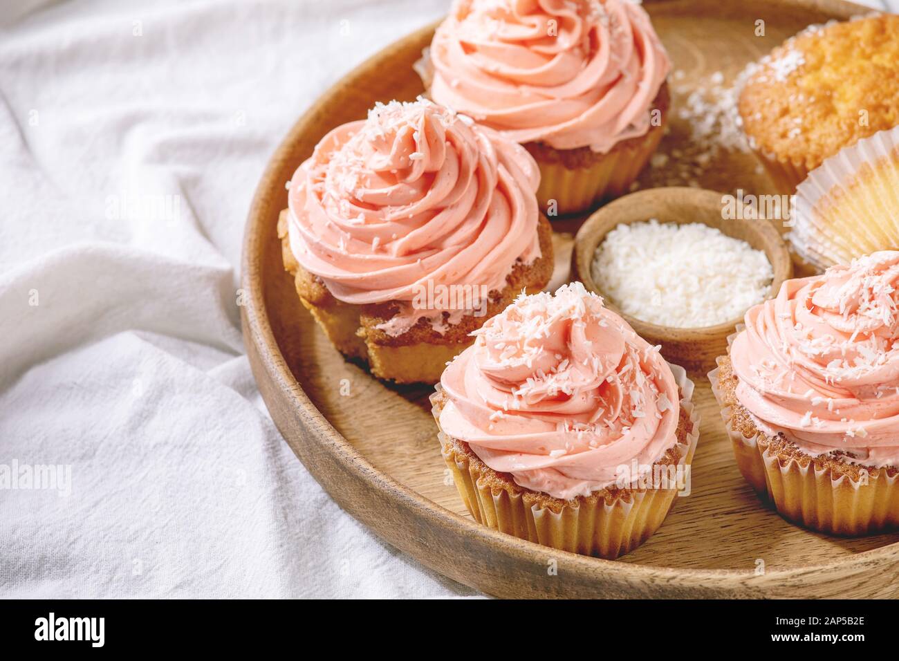 Tortini fatti in casa con la crema di burro rosa e scaglie di noce di cocco servita nel piatto di legno su bianco tovaglia ripiegata come sfondo. Close up Foto Stock