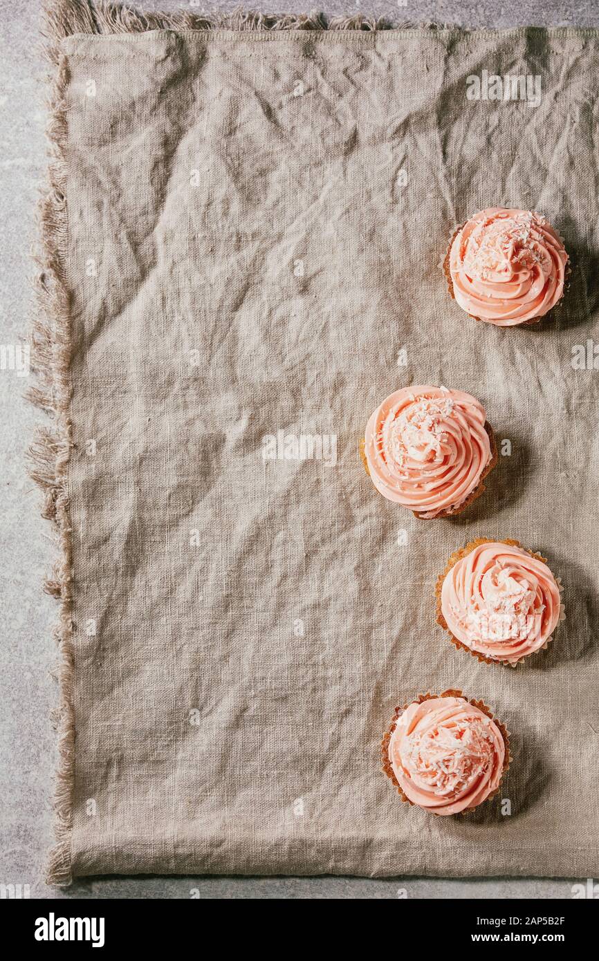 Tortini fatti in casa con la crema di burro rosa e scaglie di noce di cocco servita su piastra in ceramica grigia su tela di lino come sfondo. Laici piana, spazio Foto Stock