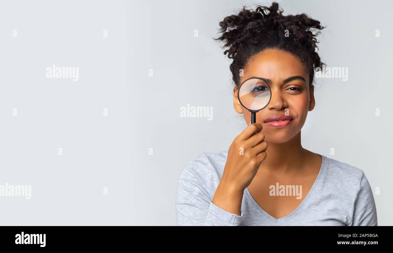 Curiosa ragazza che tiene lente di ingrandimento su sfondo grigio Foto Stock