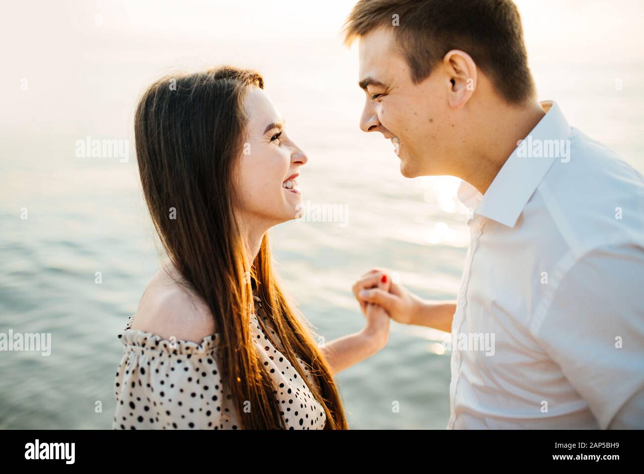 Foto di un felice coccole al tramonto vicino al mare. Bella donna e bell'uomo che si guardano, allegramente ridendo. Foto Stock