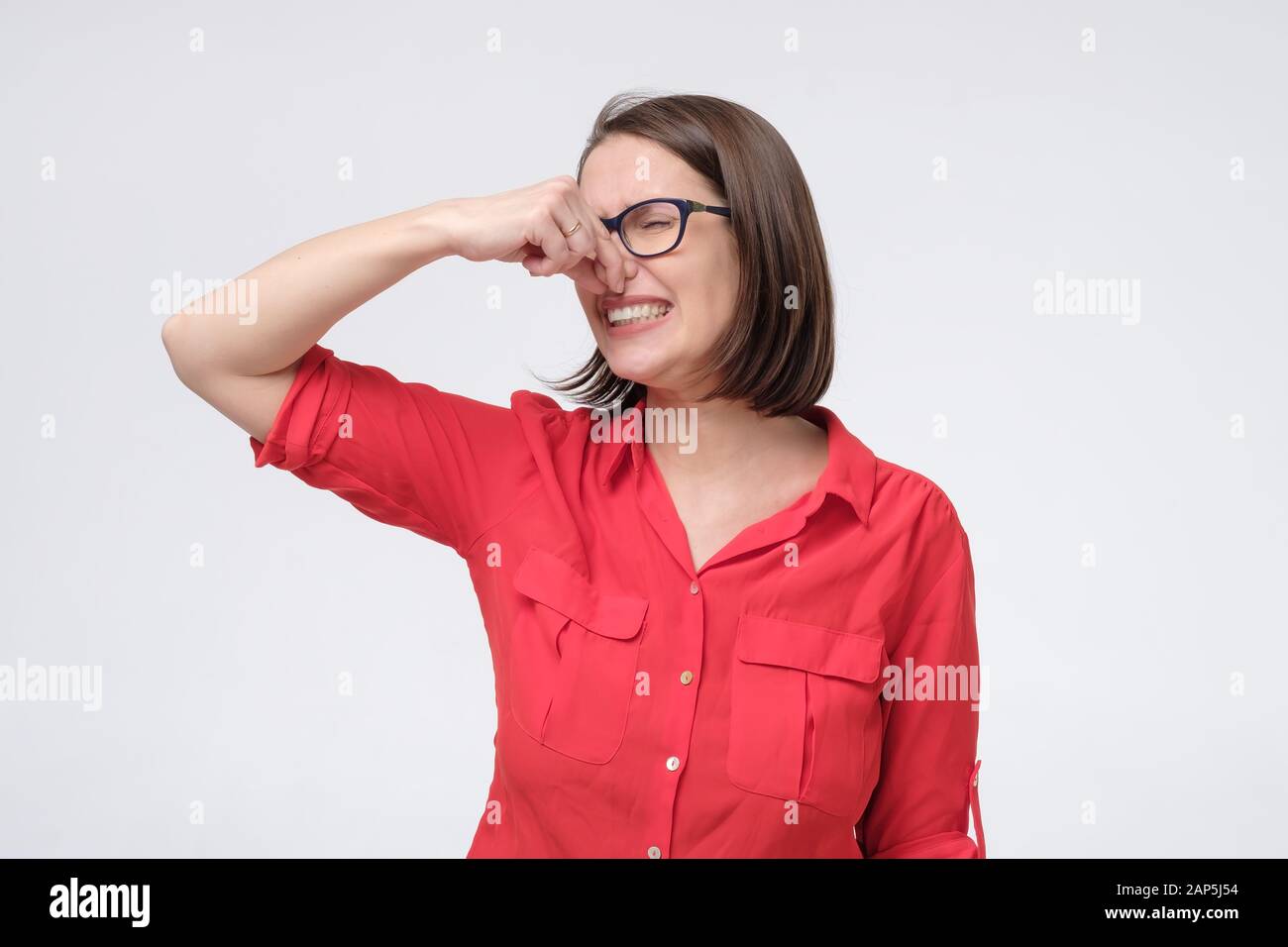 L'uomo caucasico maturo nei vetri e nei tappi rossi della camicia vicino il naso con le dita ritiene il profumo sgradevole soffre dal pustench che pone isolato sullo studio grigio Foto Stock
