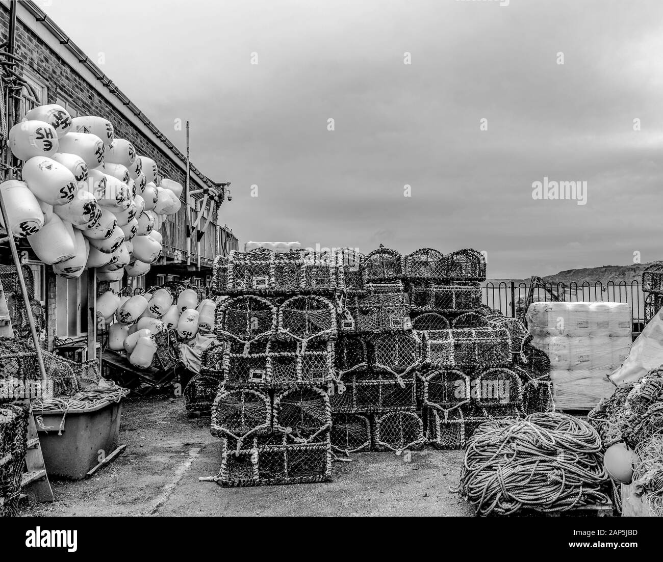 Deposito dei pescatori con vasetti, reti, funi e boe di aragosta. C'è un promontorio in lontananza e un cielo nuvoloso sopra. Foto Stock