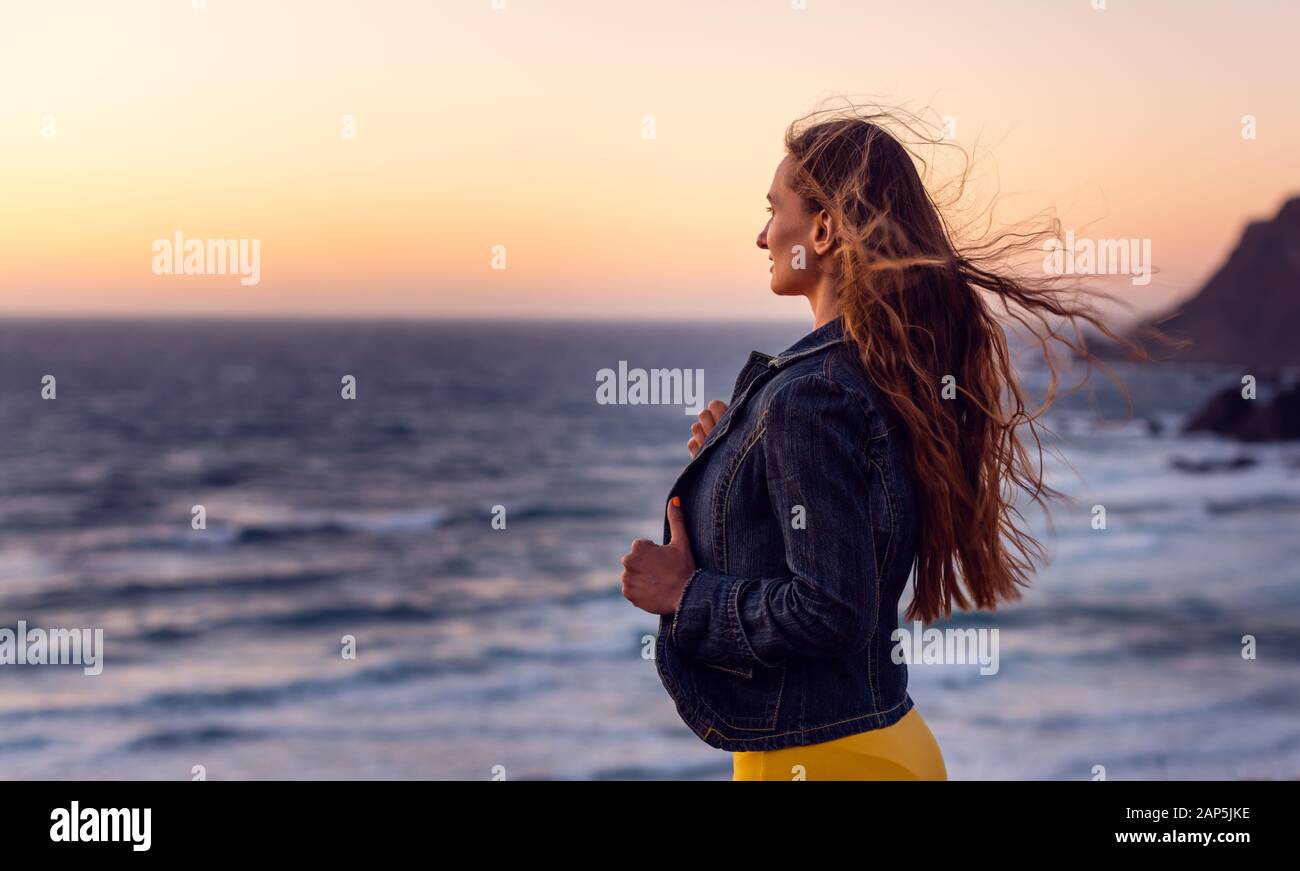 Una donna su una spiaggia al tramonto con il vento tra i capelli Foto Stock