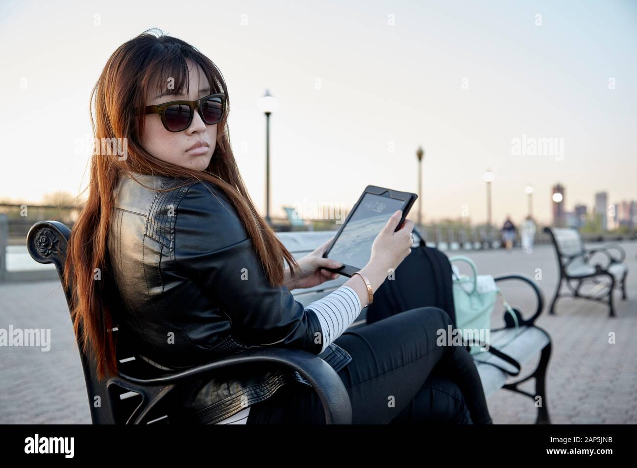 Donna asiatica seduta sulla panchina usando un tablet e indossando occhiali da sole Foto Stock