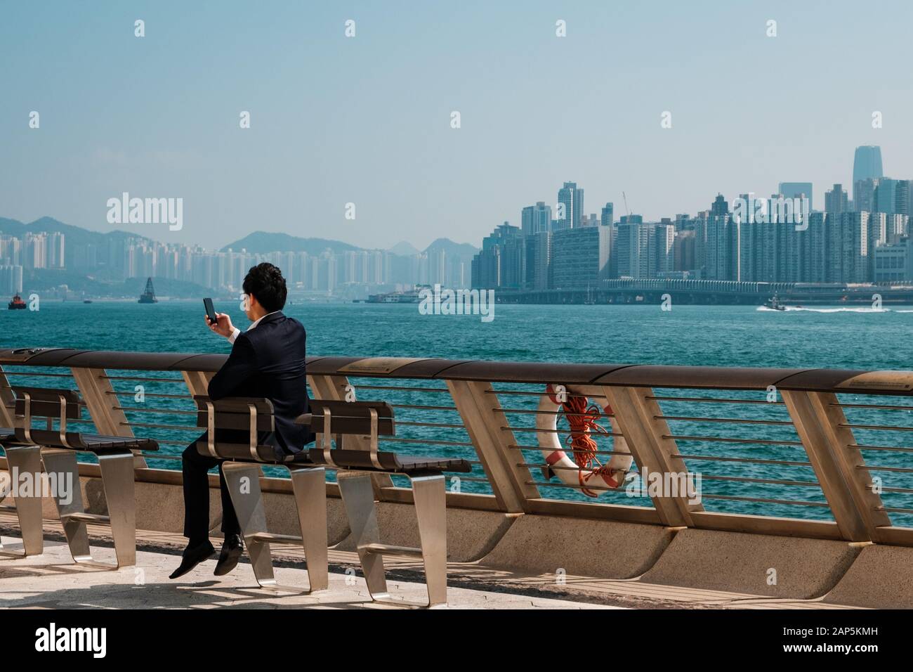 Imprenditore guardando smart telefono cellulare all'aperto con lo sfondo dello skyline di Hong Kong Foto Stock