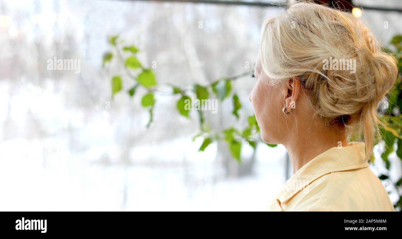 Biondo anonimo che guarda attraverso la finestra Foto Stock