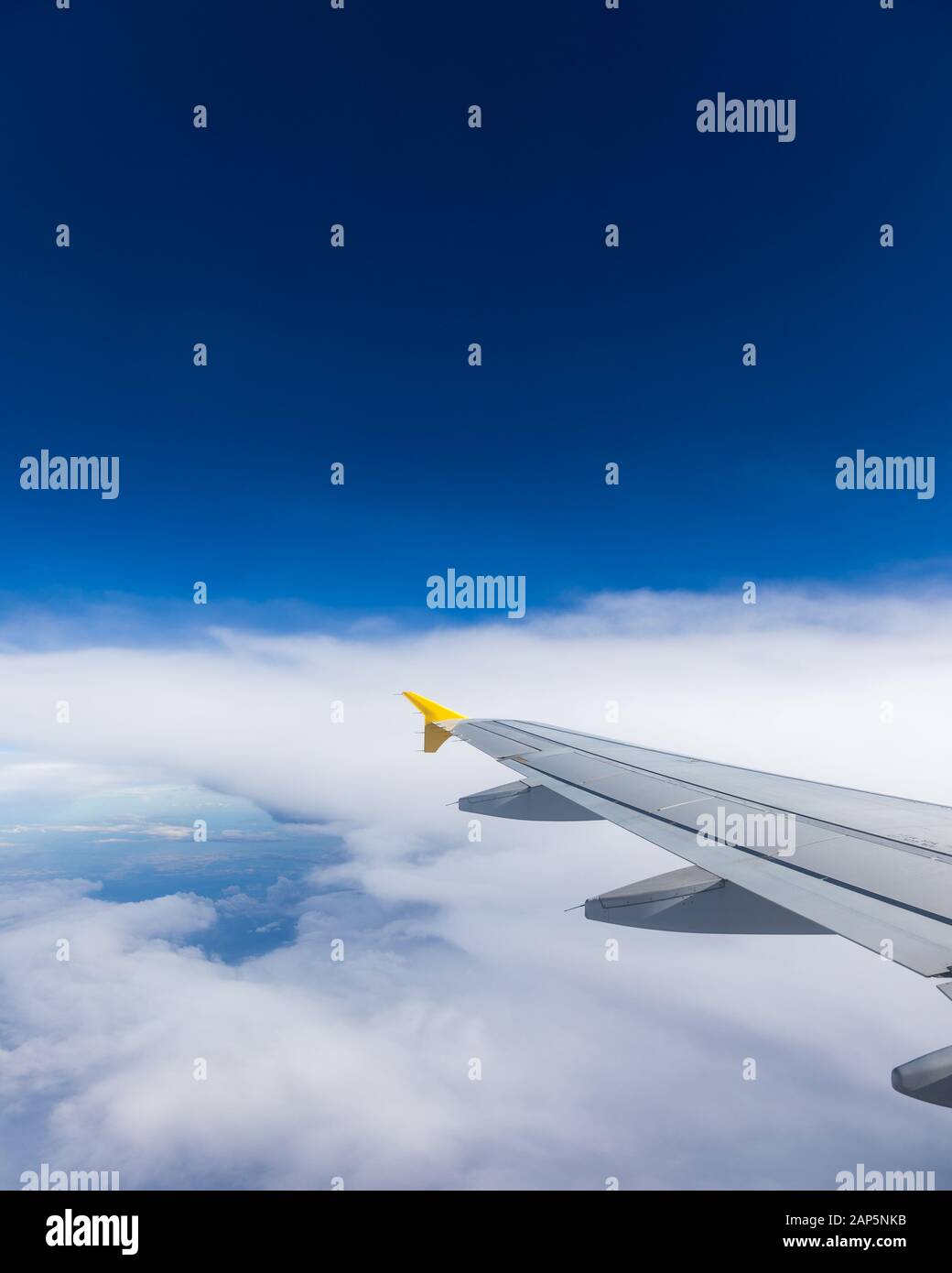 Vista di un'ala di aeroplano che vola sopra le nuvole ad alta altitudine sotto un cielo blu dall'alzavetro passeggero. In volo sopra l'Europa. Vista di je Foto Stock