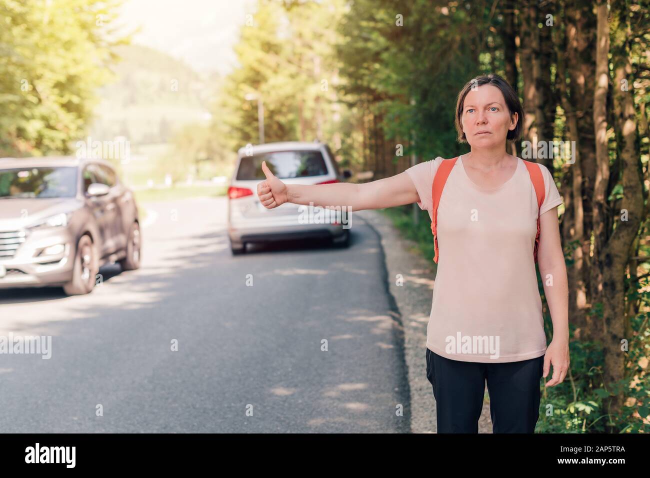 Escursionista femmina autostop su strada attraverso la campagna sulla soleggiata giornata estiva Foto Stock