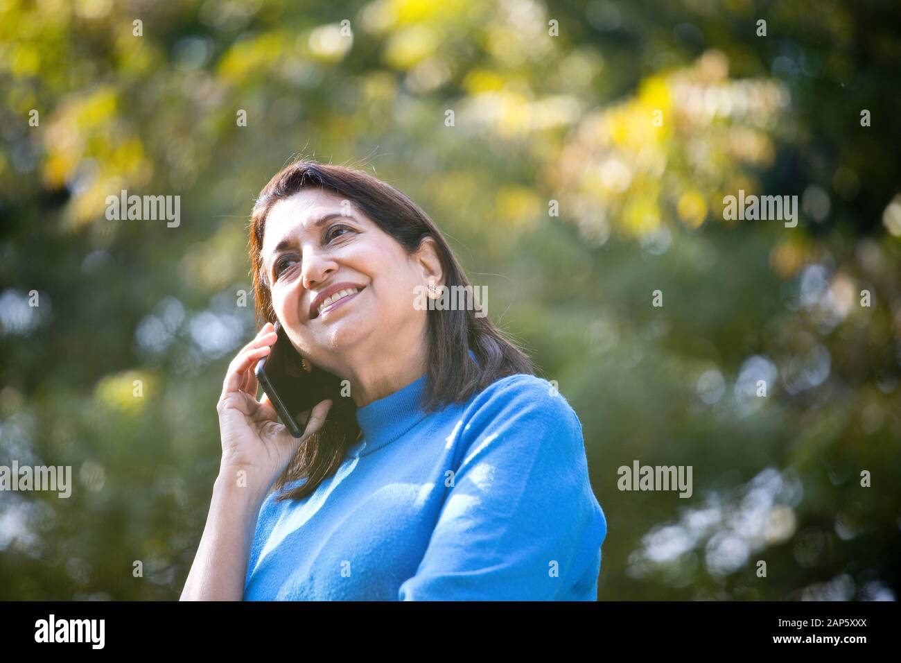 Donna anziana felice che usa il telefono al parco Foto Stock