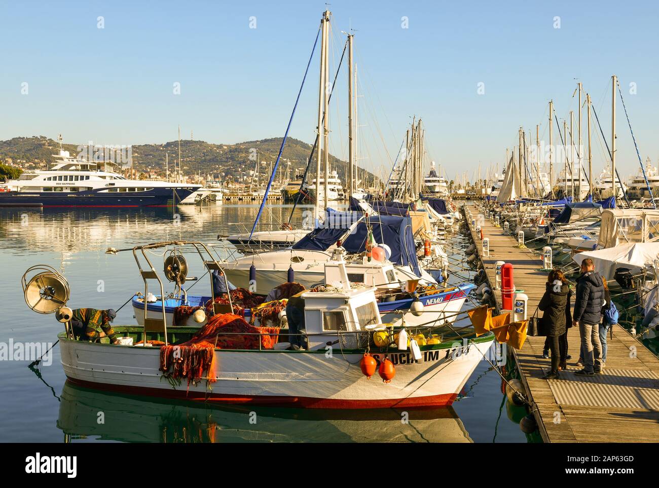 Persone in attesa di acquistare pesce direttamente da un pescatore su un molo del porto in una giornata di sole, Porto Maurizio, Imperia, Liguria, Italia Foto Stock
