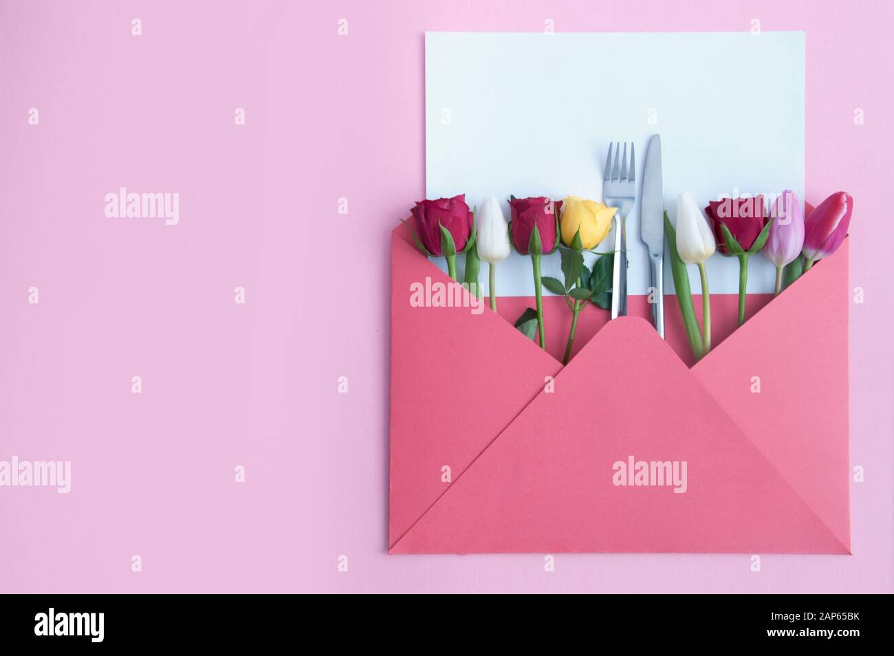 Busta con rose assortite e tulipani e coltello e forchetta al centro con foglio di carta bianco Foto Stock