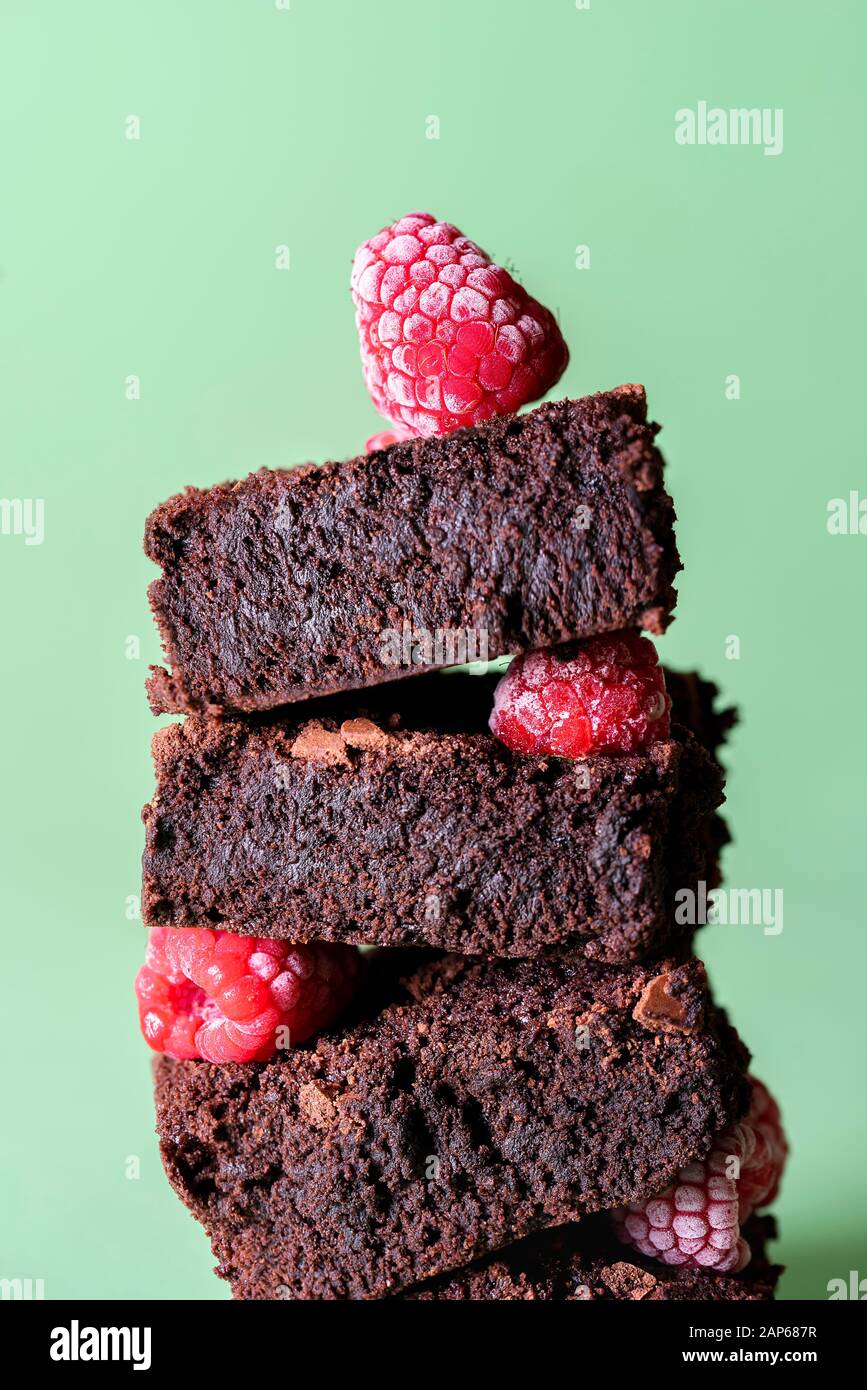 Cioccolato brownie primo piano in una pila con frutti di bosco congelati su sfondo verde. Torte di cacao saporite. Mucchio di brownies e lamponi. Dessert al cioccolato. Foto Stock