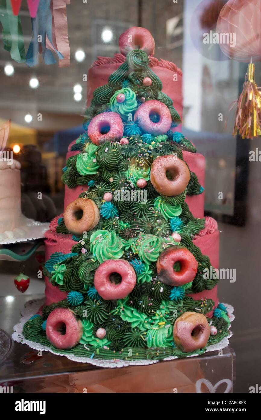 Una torta colorata a forma di albero di Natale viene visualizzata in una finestra del negozio. Foto Stock