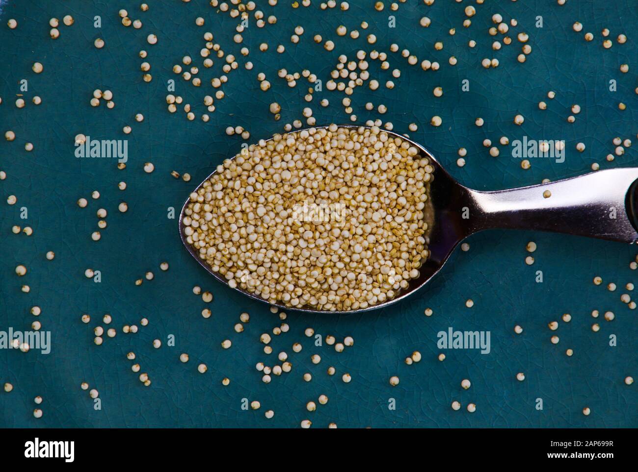 Primo piano di cucchiaio d'argento isolato pieno di semi di quinoa su vecchio piatto di porcellana graffiato blu Foto Stock