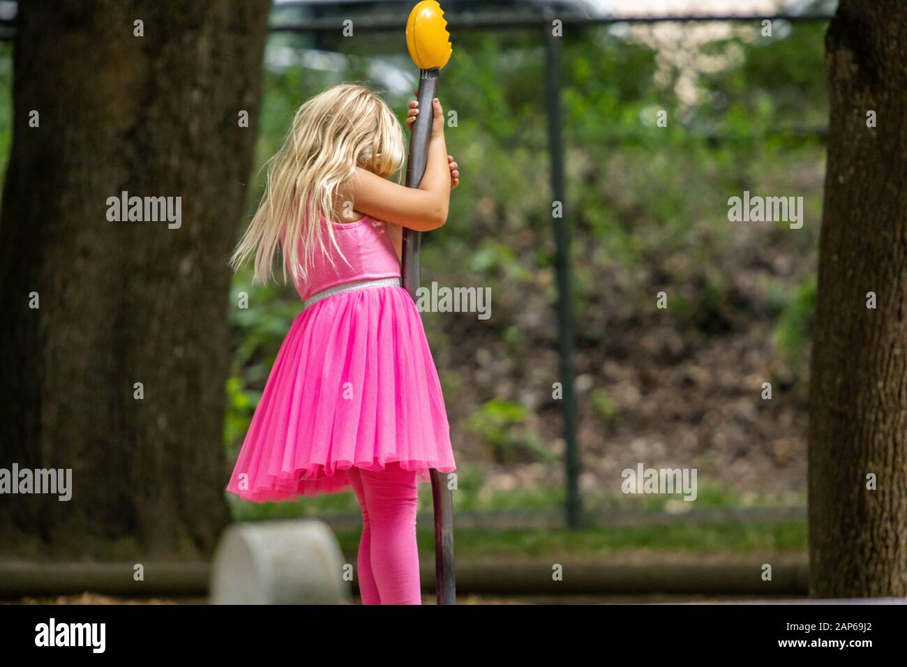 Ragazza con i capelli biondi aperti che indossano vestito rosa e leggings  mentre gioca e tiene palo nero di plastica contro gli alberi nel parco Foto  stock - Alamy
