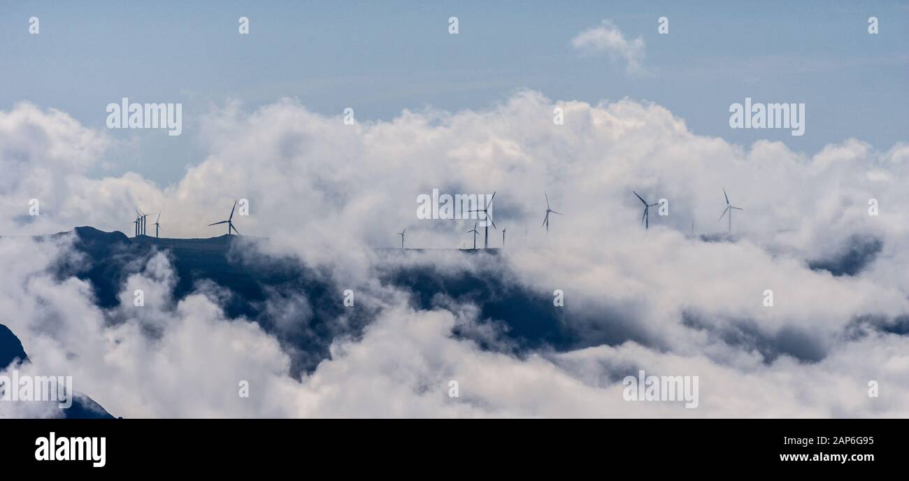 Centrale eolica installata sulla cima della montagna con nuvole drammatiche Foto Stock