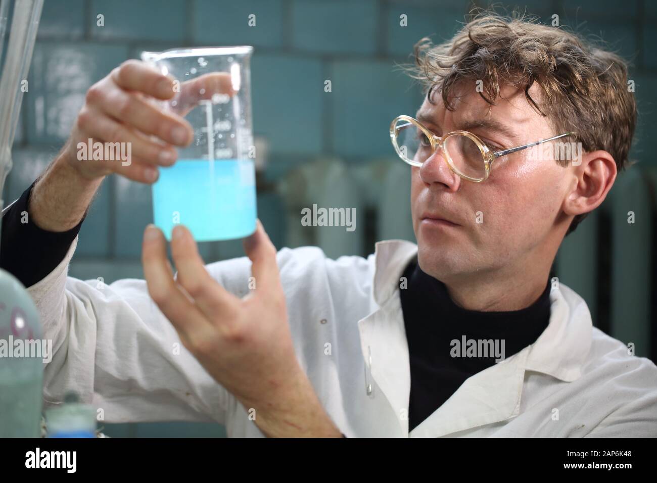 Uno scienziato in camice bianco sta tenendo in mano un bicchiere con un reagente di blu Foto Stock