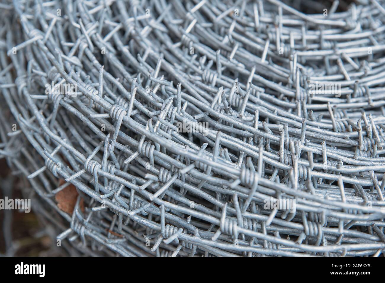 Primo piano su un rotolo di pile di nuovo filo spinato lucido per recinzione recinto. Protezione della sicurezza applicazione della legge. Carcere reato penale bloccato. Foto Stock