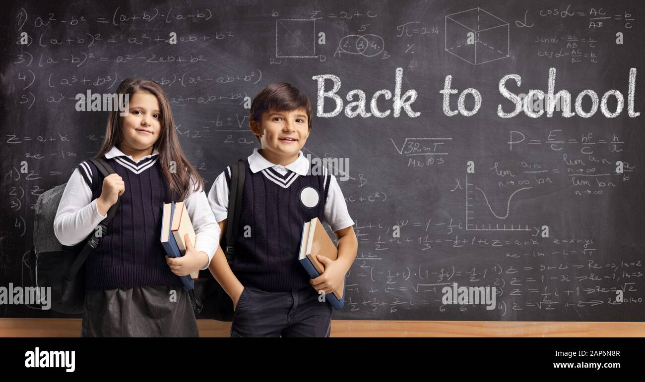 Un ragazzo e una ragazza in uniformi di scuola in piedi di fronte a una lavagna con formule matematiche e testo scritto si torna a scuola Foto Stock
