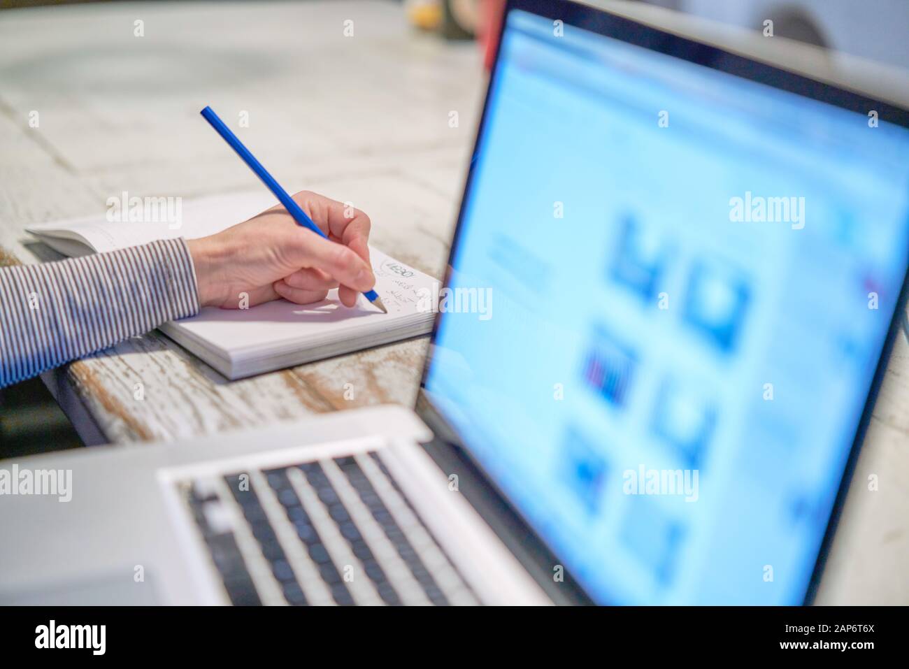 Closeup del braccio della mano della donna che scrive lavorando con una penna  su un documento vicino al suo PC portatile del calcolatore nel suo ufficio  domestico sul suo allievo del posto