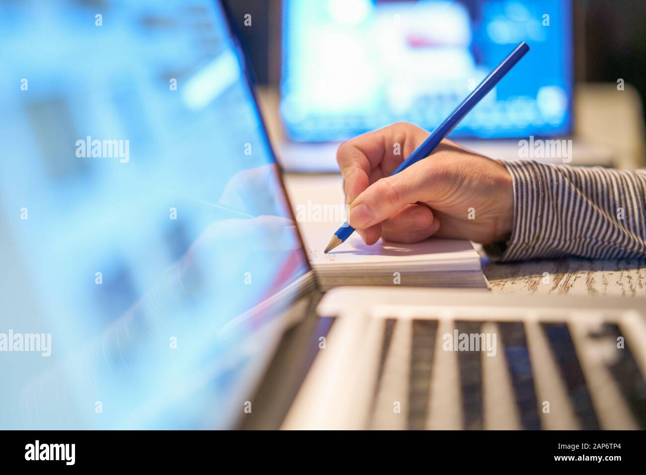 Closeup del braccio della mano della donna che scrive lavorando con una penna  su un documento vicino al suo PC portatile del calcolatore nel suo ufficio  domestico sul suo allievo del posto