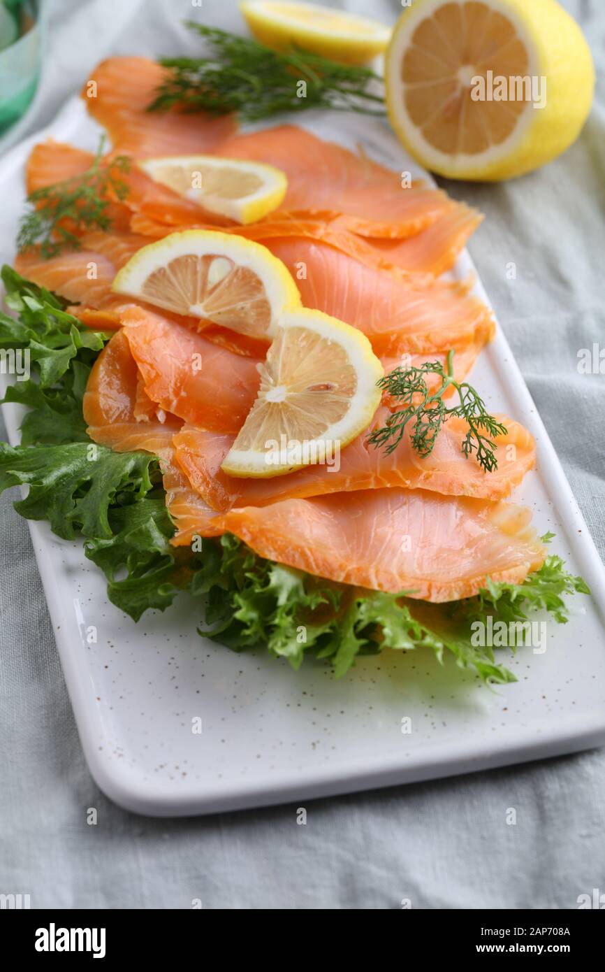 Fette di Salmone affumicato con lattuga e fette di limone su un tagliere Foto Stock