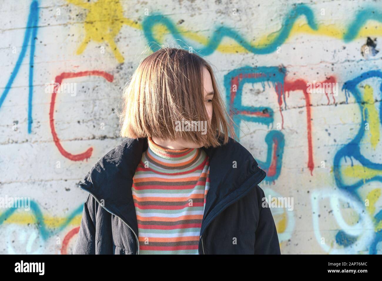 Bella ragazza adolescente con capelli corti che posano vicino alla parete graffiti. Urbano all'aperto, stile di vita adolescente Foto Stock