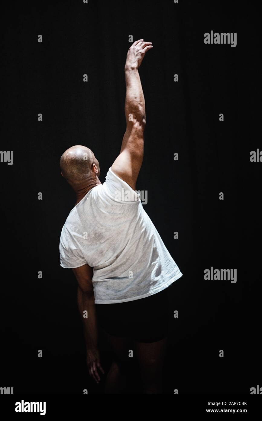 Guardando lontano dalla fotocamera Performance Artist Dances contro il nero Foto Stock