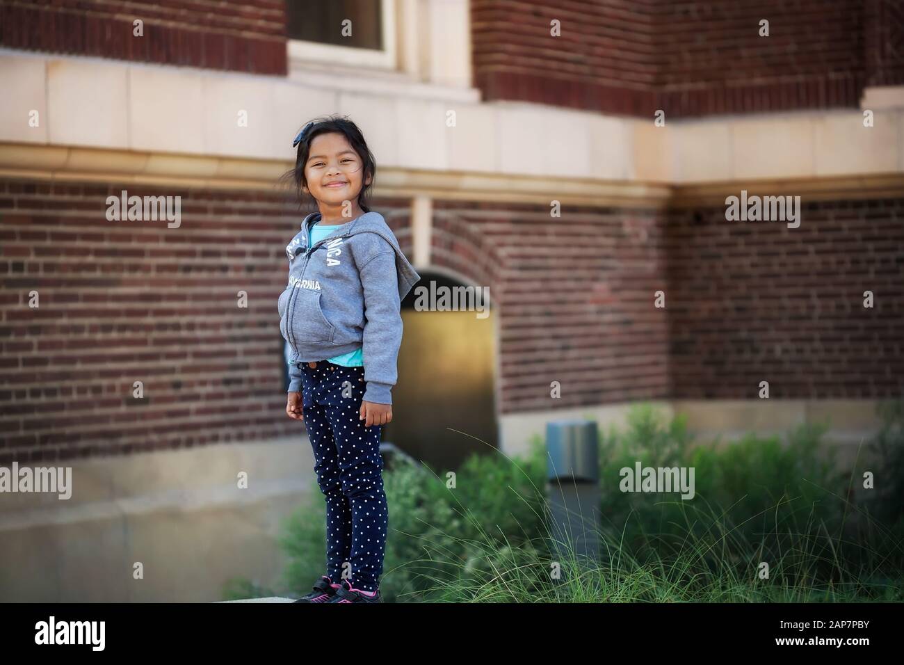 Elegante e sicuro guardando bambina, in piedi alto di fronte a un edificio scolastico fatto di mattoni. Foto Stock