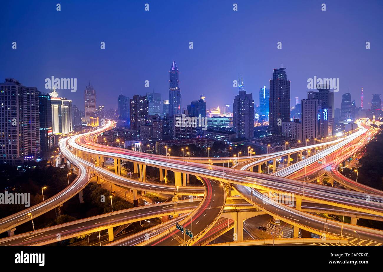 Il traffico cittadino di Shanghai si sposta in un incrocio trafficato circondato da alti edifici moderni di notte, Cina Foto Stock