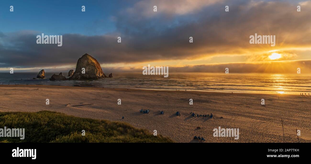 Tramonto panorama di Cannon Beach con Haystack Rock e raggi del sole. Foto Stock