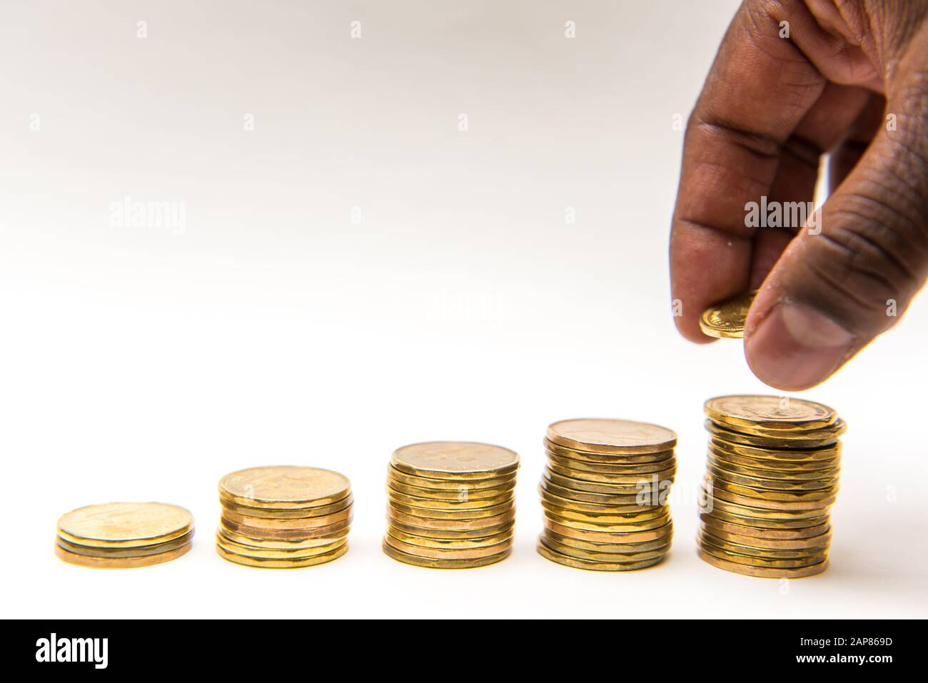 Monete canadesi in dollari saccheggiate in cinque pile ascendenti su sfondo bianco. Mano può essere visto prendere o aggiungere una moneta al palo. Foto Stock