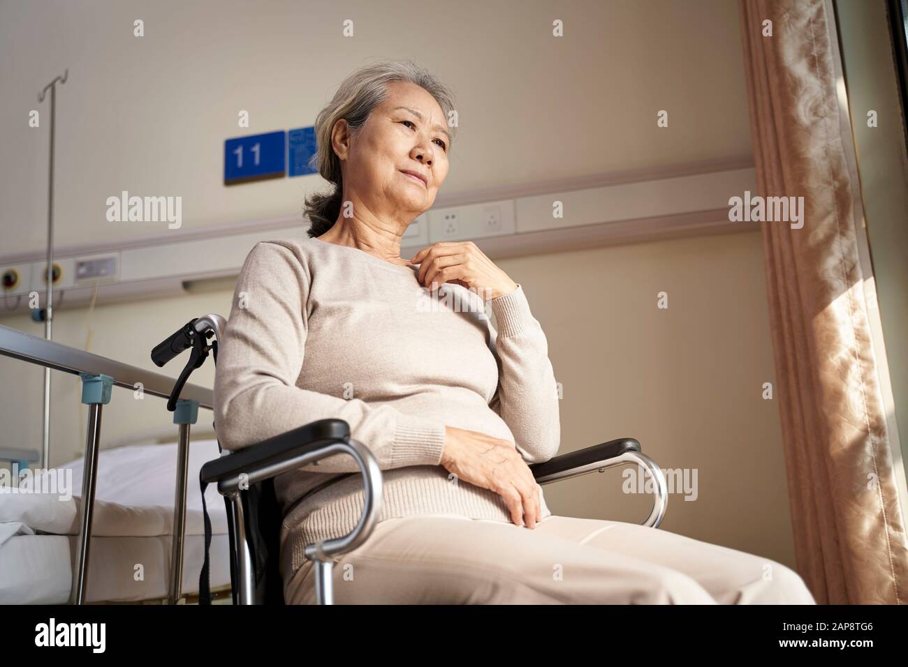 triste e depresso donna asiatica senior seduta da sola in sedia a rotelle in casa di cura Foto Stock