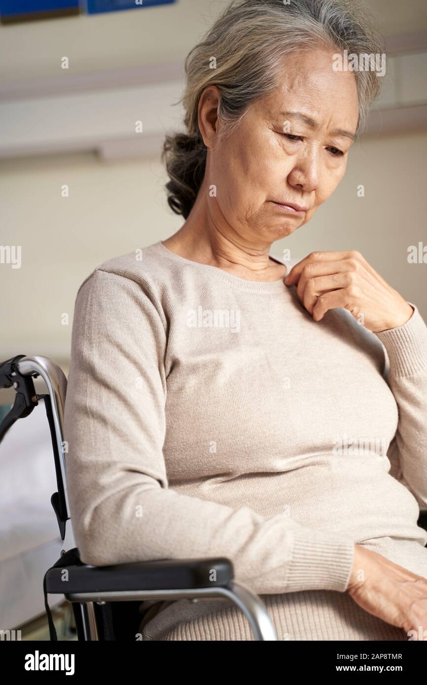 triste e depressa asiatica vecchia donna seduta da sola in sedia a rotelle con testa giù in casa di cura Foto Stock