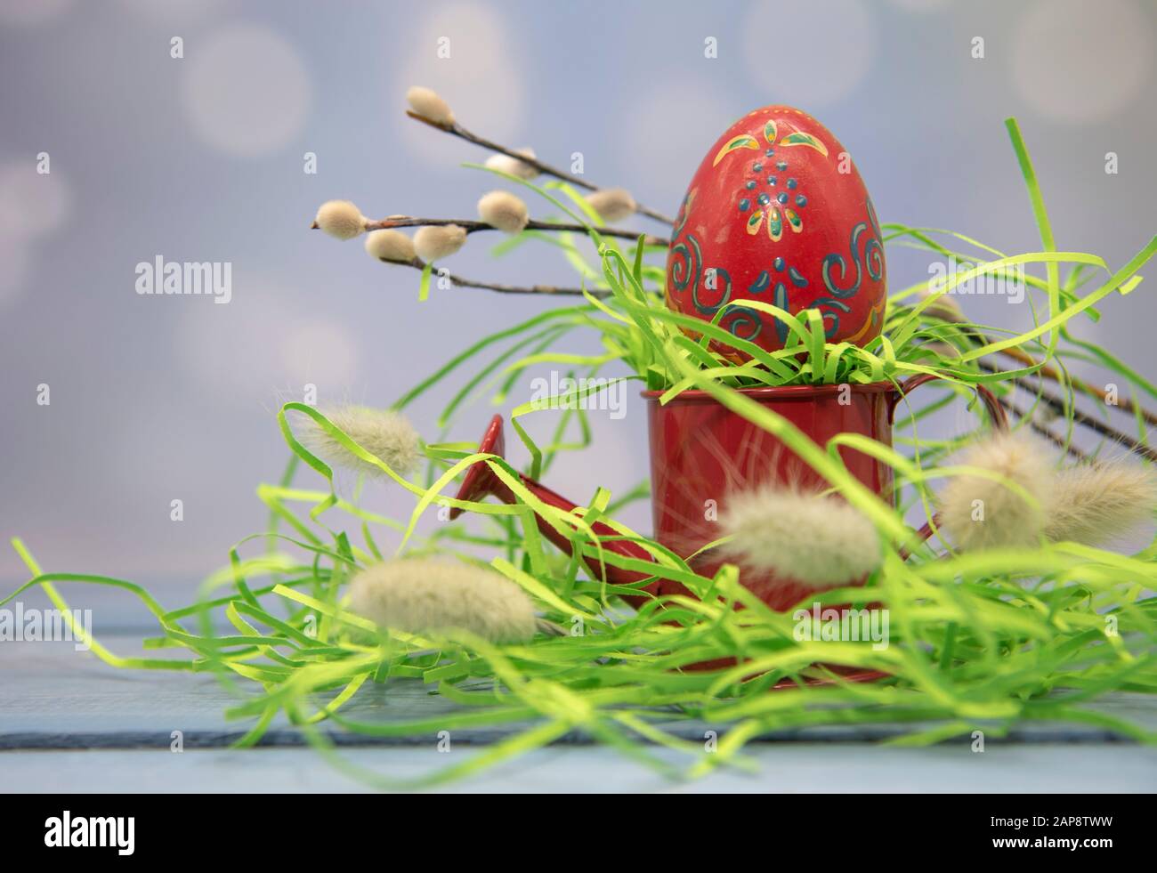 Un uovo di pasqua si erge su una piccola annaffiatura rossa come su uno stand su uno sfondo sfocato. Foto Stock