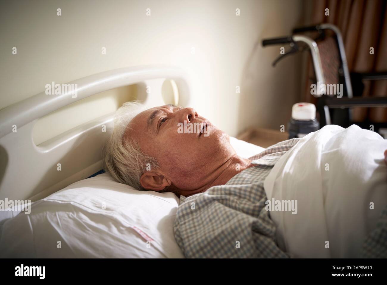 l'uomo asiatico anziano malato che giace nel letto dell'ospedale sembra essere triste e indifeso Foto Stock