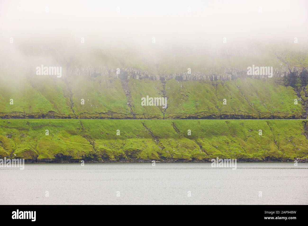 Pittoresco paesaggio verde delle isole Faroe con nebbia oceano e strada Foto Stock