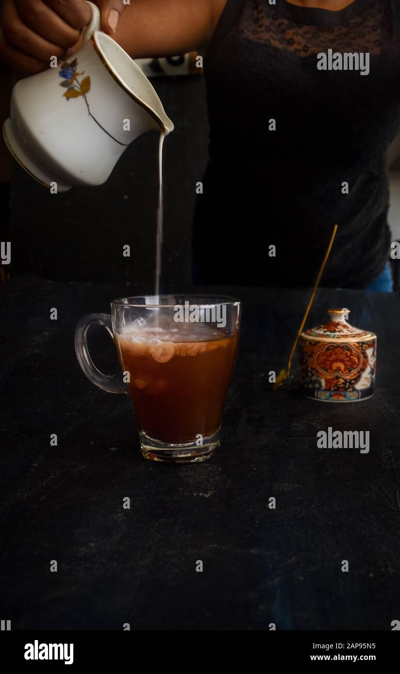 Mano di donna che versava il latte nel caffè, con il vaso di zucchero sullo sfondo. Stile loft Instagram pour shot. Latte di mandorle versato nel caffè vegano, versare sopra Foto Stock