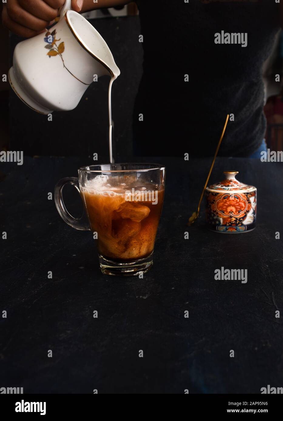 Mano di donna che versava il latte nel caffè, con il vaso di zucchero sullo sfondo. Stile loft Instagram pour shot. Latte di mandorle versato nel caffè vegano, Foto Stock