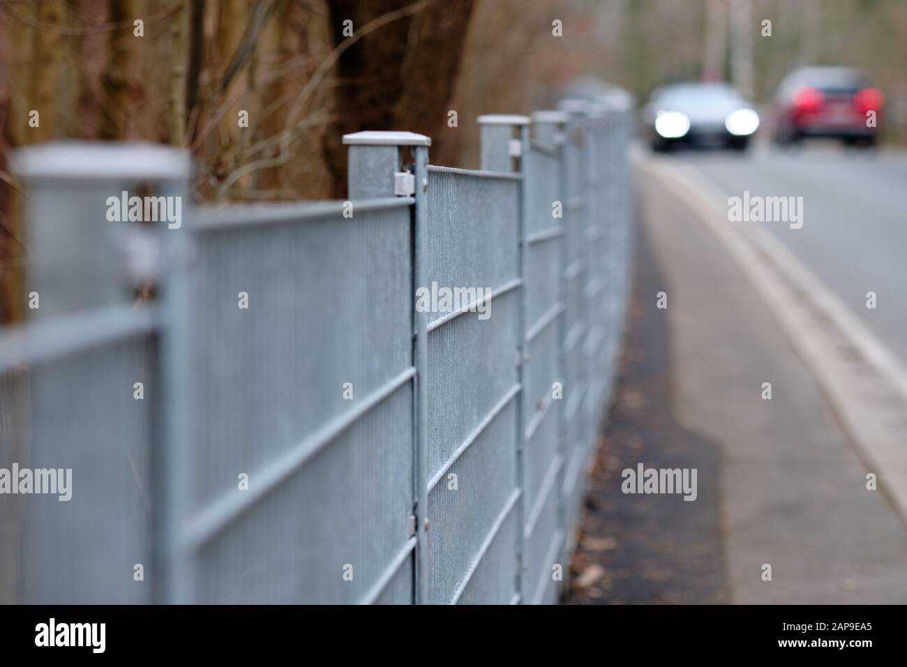 Lungo recinto grigio di stuoia di asta fatto di acciaio accanto al pavimento e una strada con le automobili che passano lungo. Visto in Germania in una giornata invernale molto intensa. Foto Stock