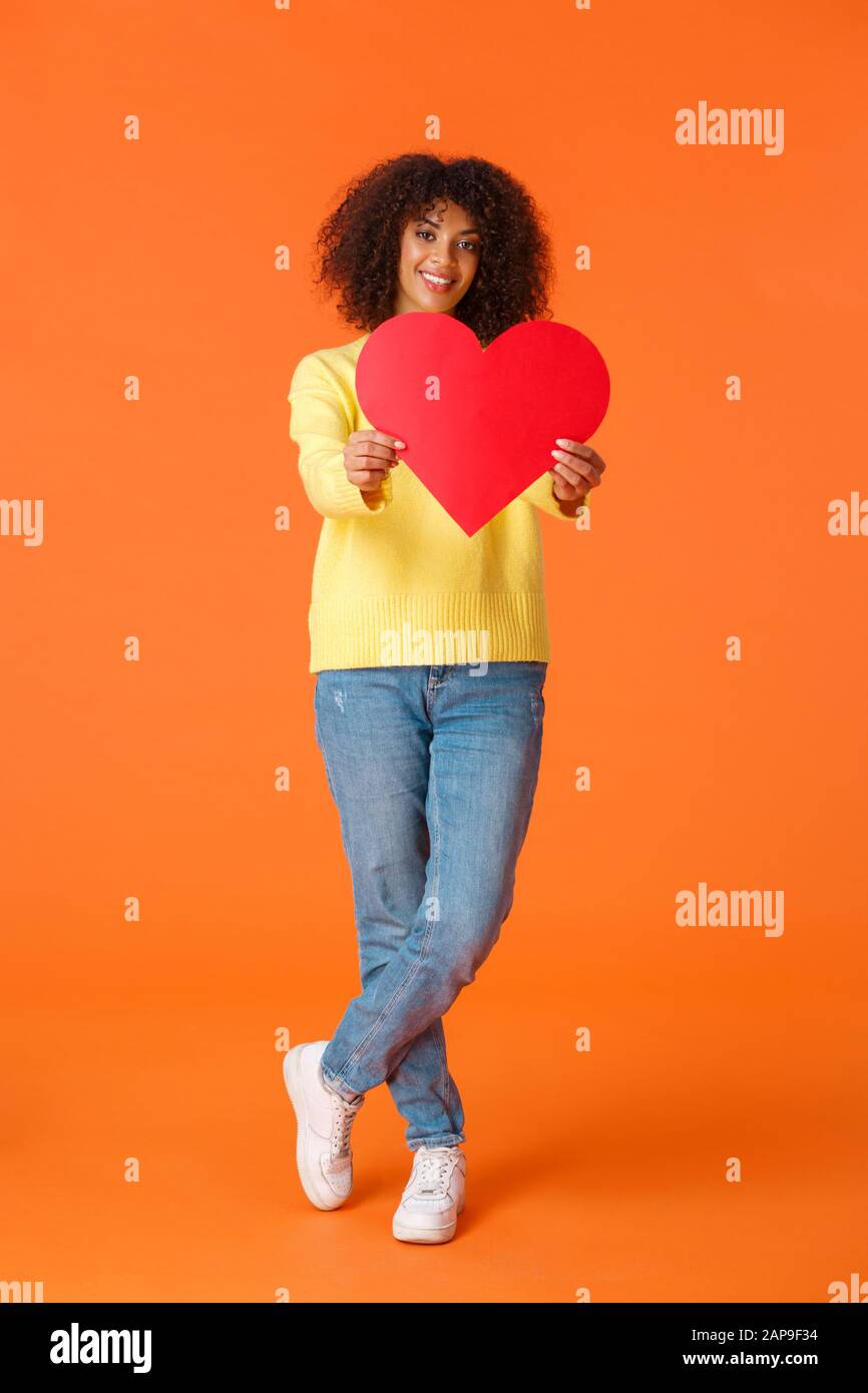 Full-lunghezza verticale scatto romantico sciocco e carino afroamerian ragazza, curly haircut, estendere le mani verso la fotocamera, dare carta cuore e sorridere Foto Stock