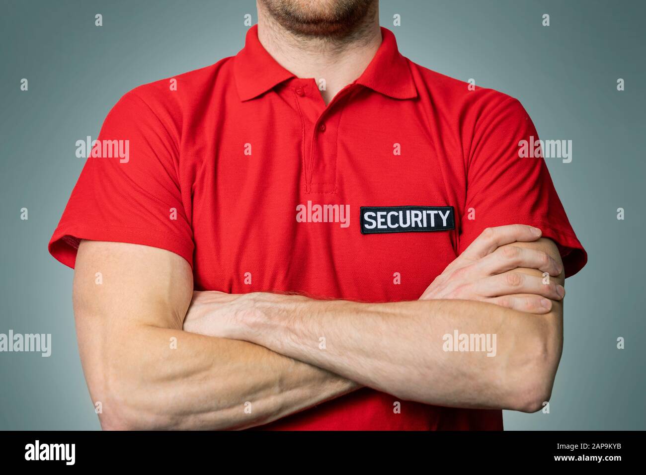 guardia di servizio di sicurezza in uniforme rossa in piedi su sfondo grigio con le braccia incrociate Foto Stock