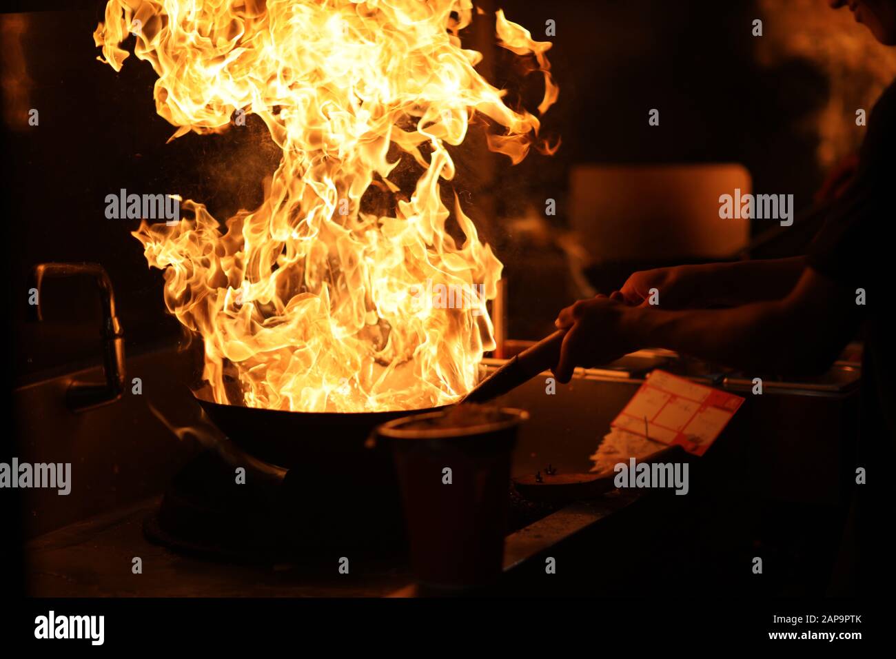 Il cuoco in cucina tiene un wok con una fiamma aperta nelle sue mani Foto Stock Il cuoco in cucina tiene un wok con una fiamma aperta nelle sue mani Foto Stock