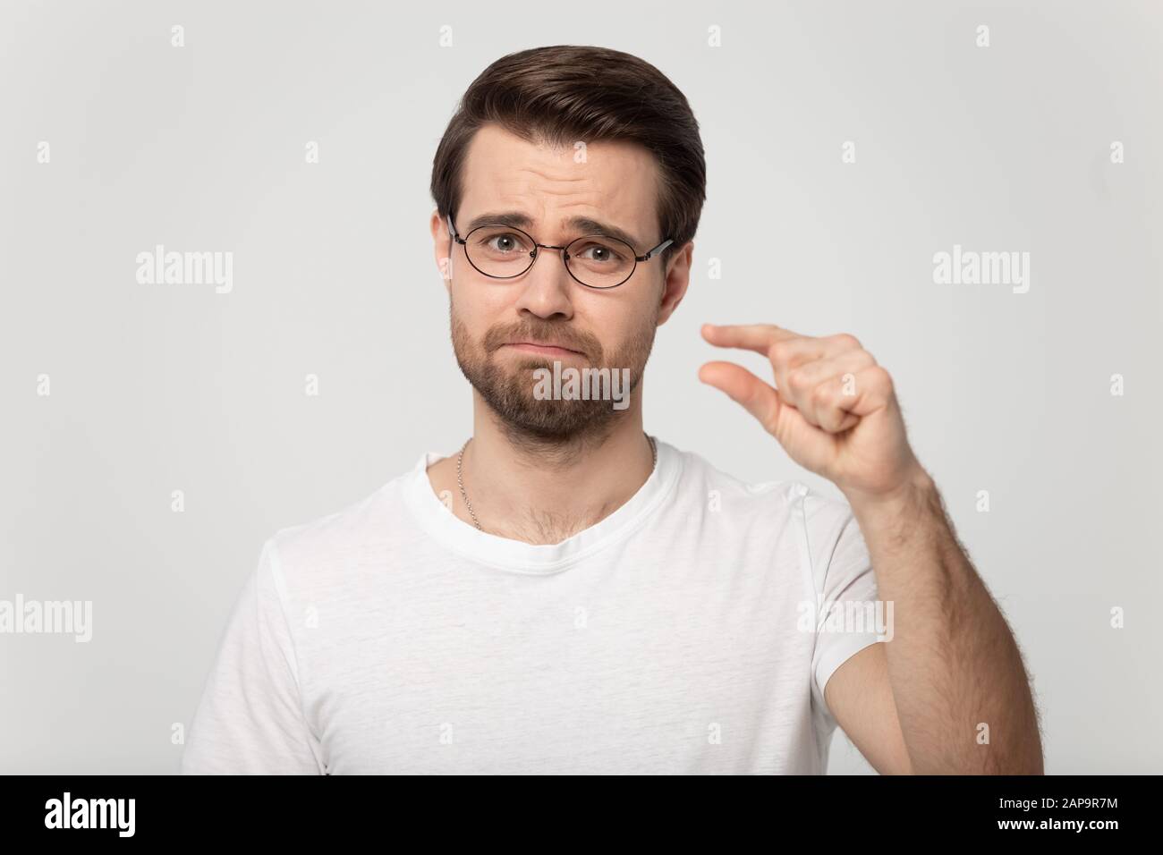 Deluso uomo millenario in bicchieri che mostra di piccole dimensioni di lunghezza. Foto Stock